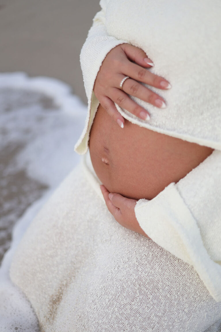 Closeup photo of a pregnant belly being held near the ocean